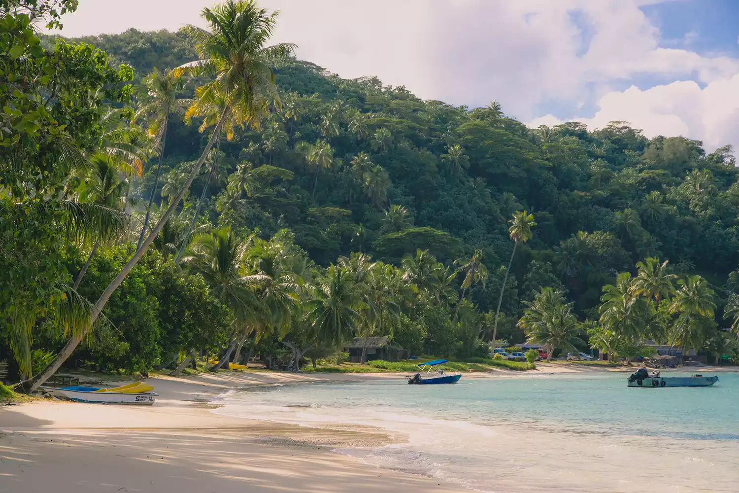 Matira Beach on Bora Bora on a sunny day with small boats and coconut palm trees.